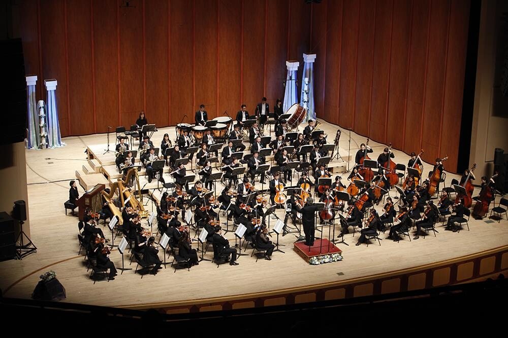 usan Symphony Orchestra performing live on stage; conductor leading the ensemble in a contemporary concert setting.